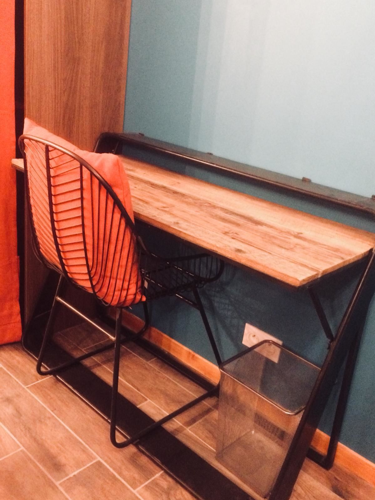Een kleine, functionele werkplek met een houten bureau en een stoel met een net rugleuning.