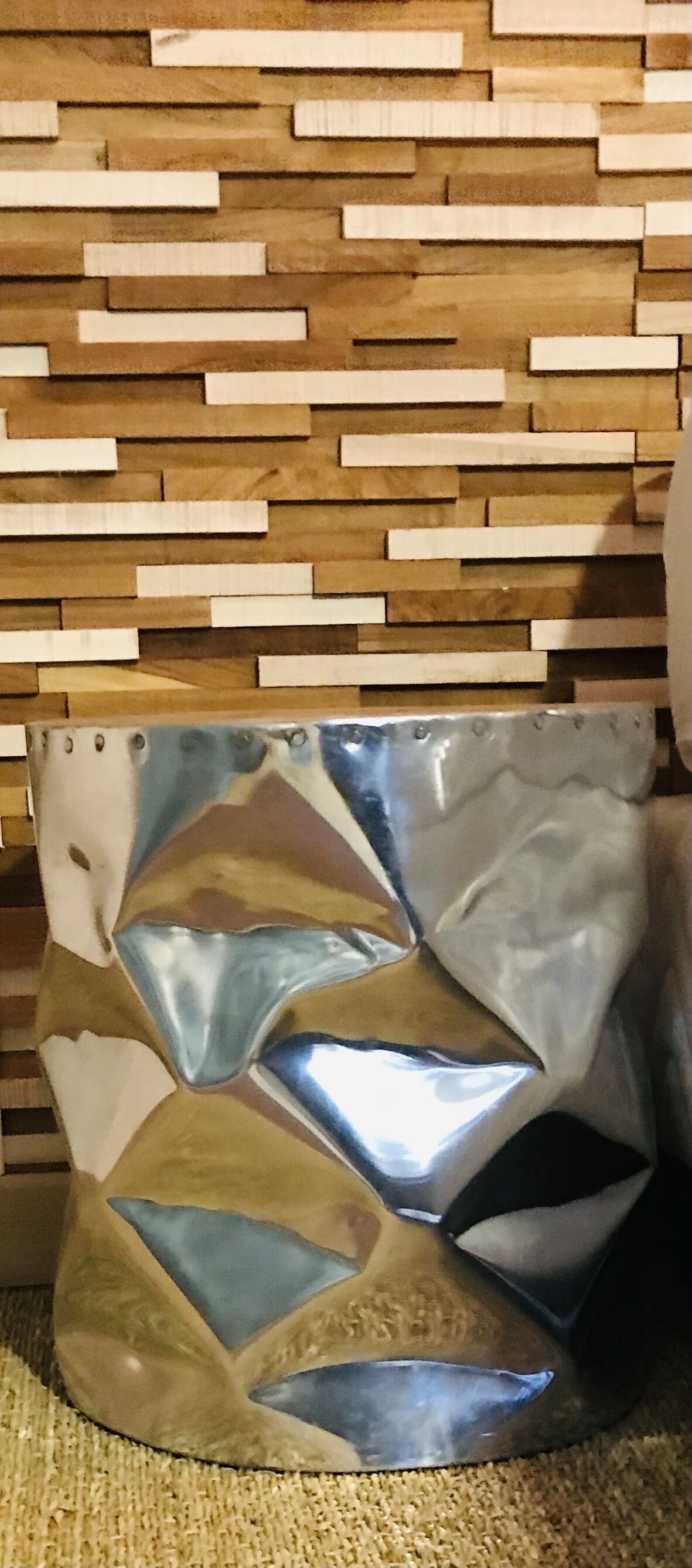 Un adorno de pared metálico y abstracto con formas geométricas frente a una pared de madera con tablones horizontales.