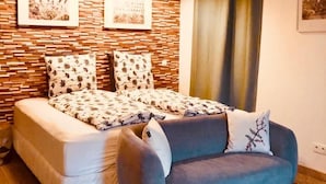Un dormitorio moderno con cama, sofá, ventilador de techo y una pared con paneles de madera y cuadros enmarcados.