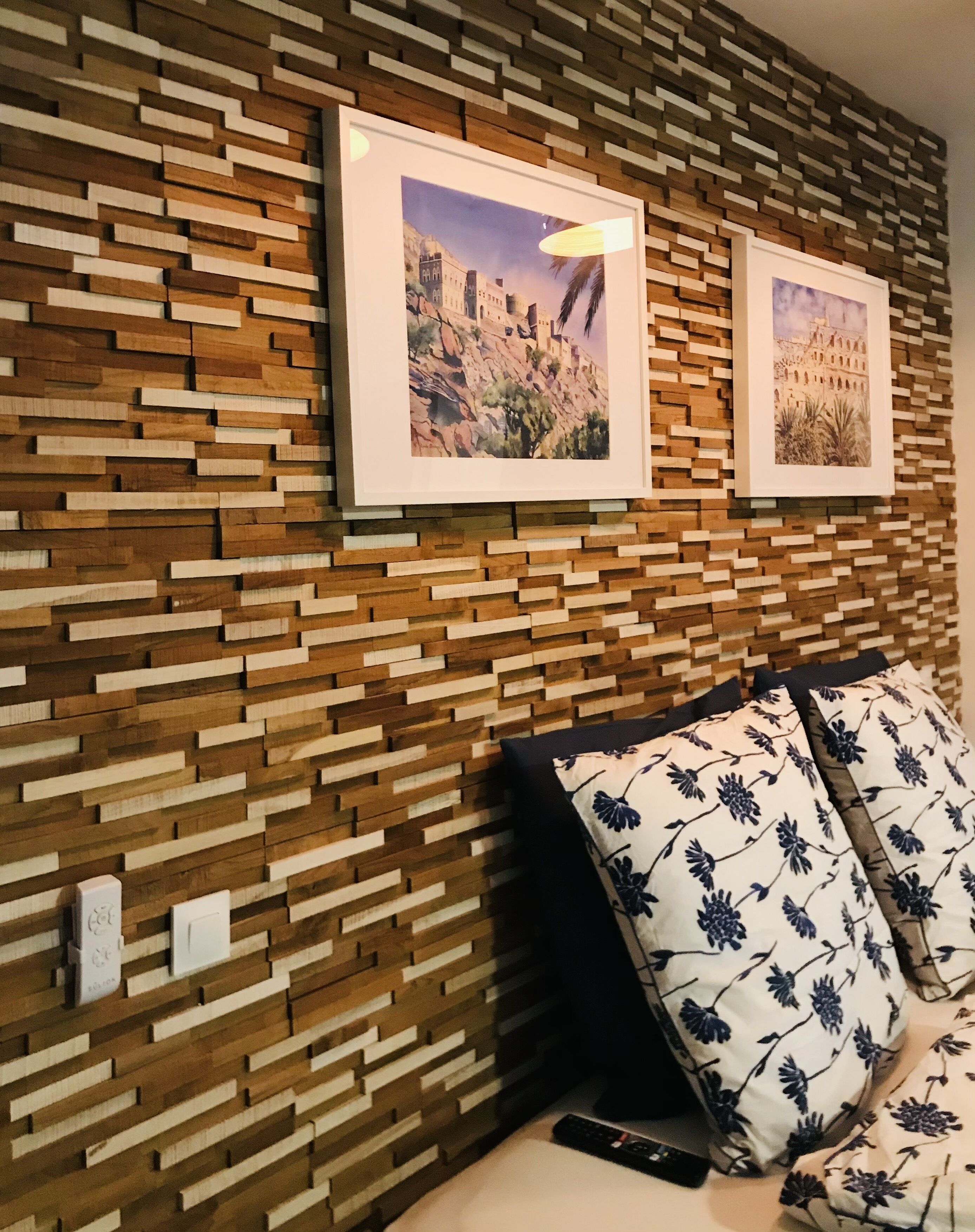 A room with a wooden wall panel design, two framed pictures, a remote control, and a pillow with a floral pattern.
