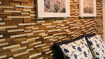 A room with a wooden wall panel design, two framed pictures, a remote control, and a pillow with a floral pattern.