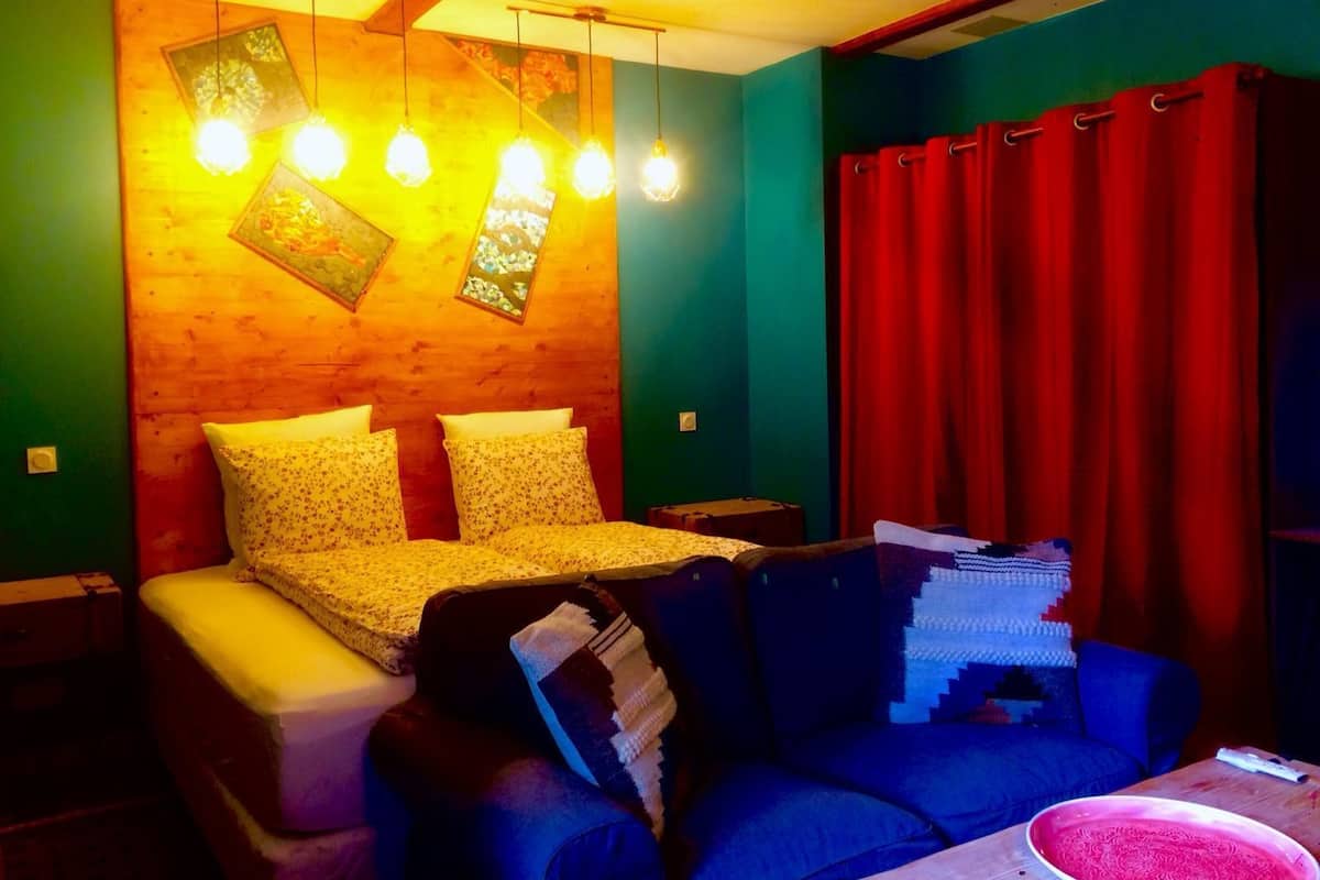 Quarto com cama, sofá e mesa. Quatro lâmpadas pendem sobre a cama.