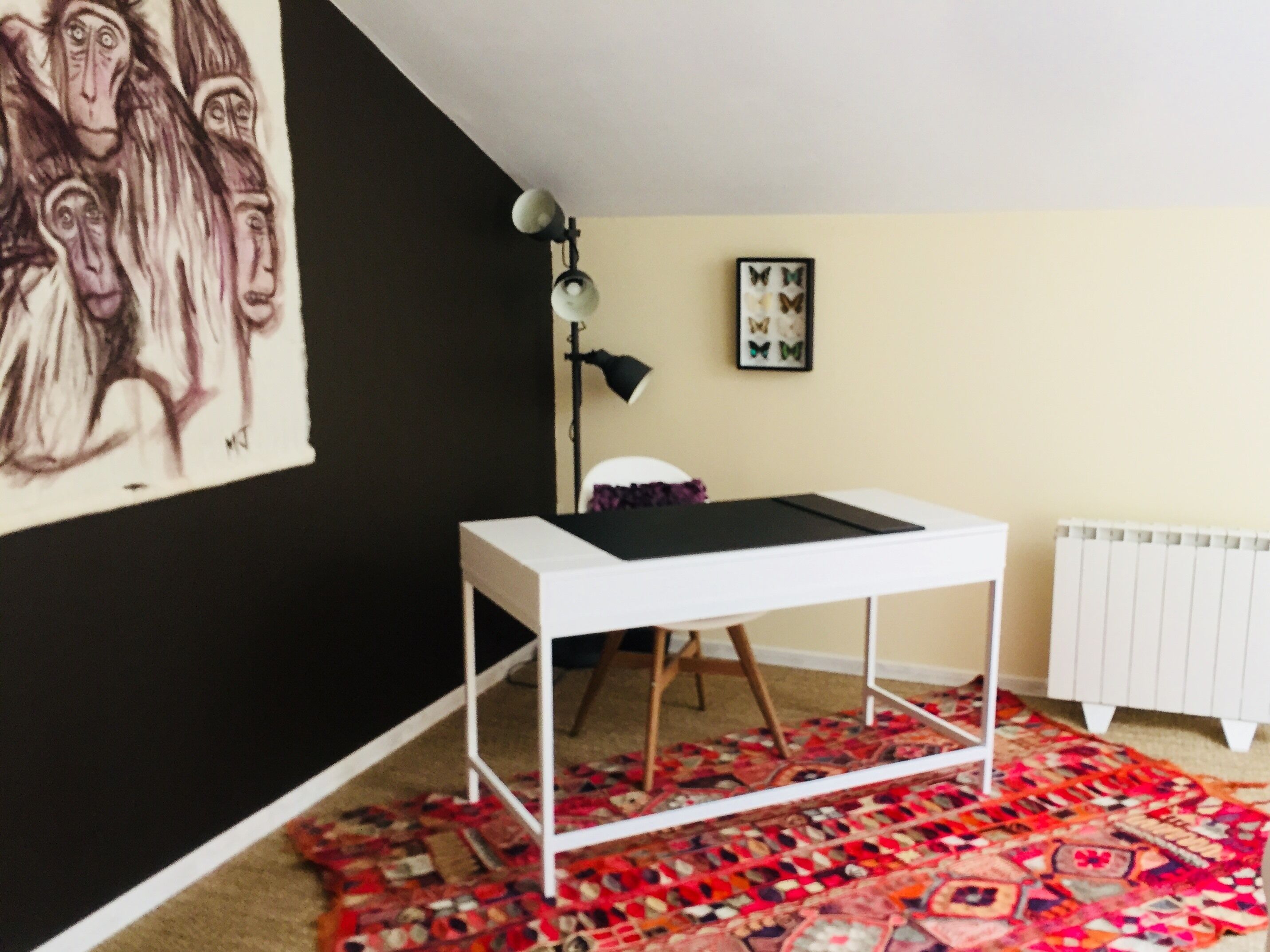 A room with a white desk, a patterned rug, a black lamp, and a radiator.