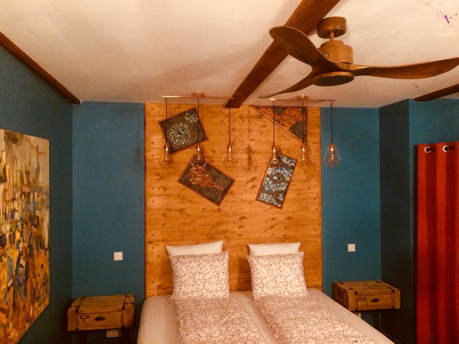 Ein Zimmer mit einem hölzernen Kopfende, einem Bett mit floraler Bettwäsche, einem Deckenventilator und einem Bild an der Wand.
