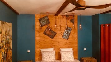 Ein Zimmer mit einem hölzernen Kopfende, einem Bett mit floraler Bettwäsche, einem Deckenventilator und einem Bild an der Wand.
