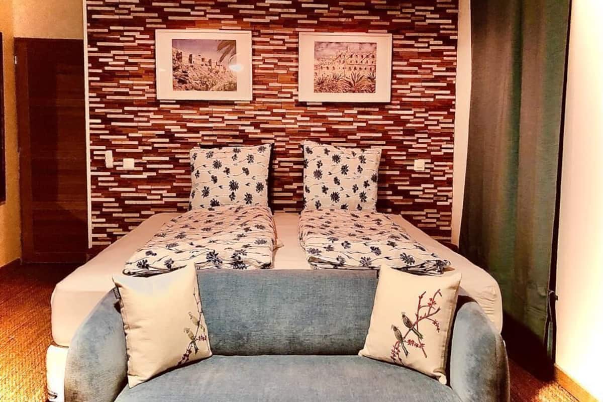 Quarto com parede estampada, duas camas com roupa de cama floral combinando, um sofá azul e duas luminárias fixadas na parede.