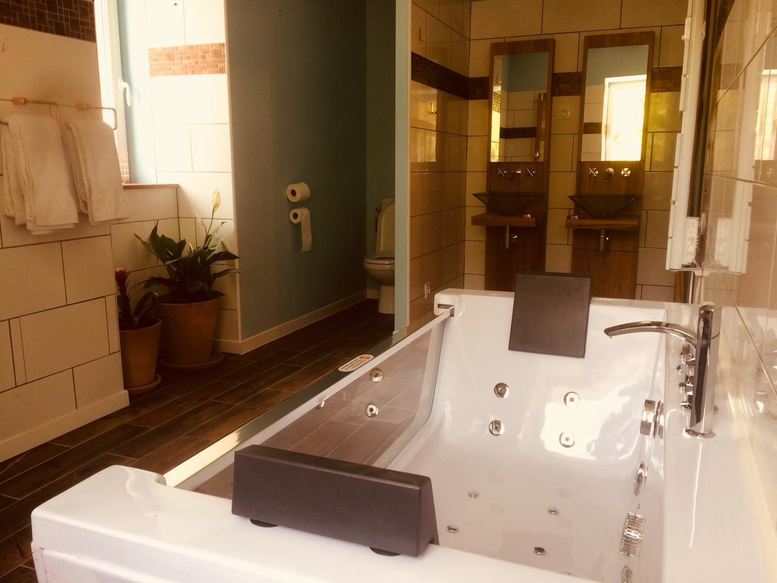 Ein modernes Badezimmer mit einer großen Badewanne, einer Toilette und einem Waschbecken. Handtücher hängen an einem Wäscheständer und eine Topfpflanze steht auf dem Boden.