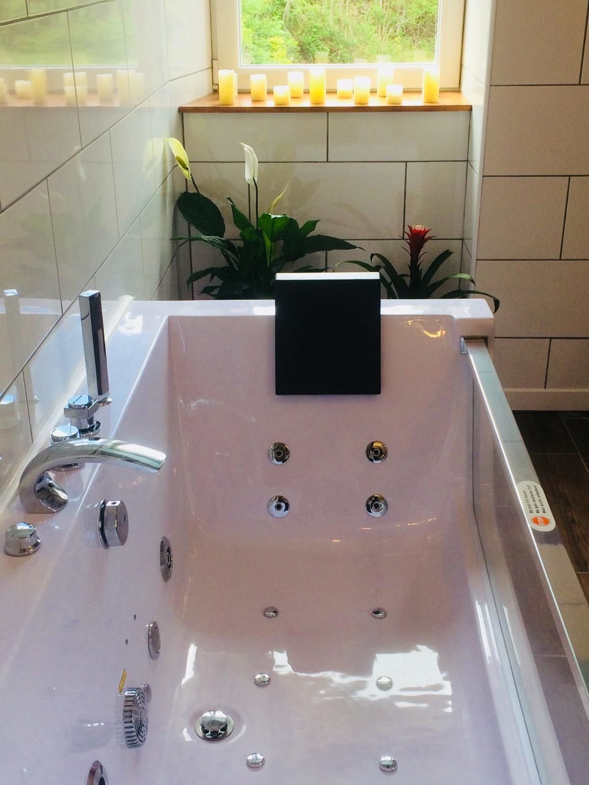 Ein modernes Badezimmer mit einer großen Badewanne, einem Fenster mit Kerzen und Topfpflanzen.
