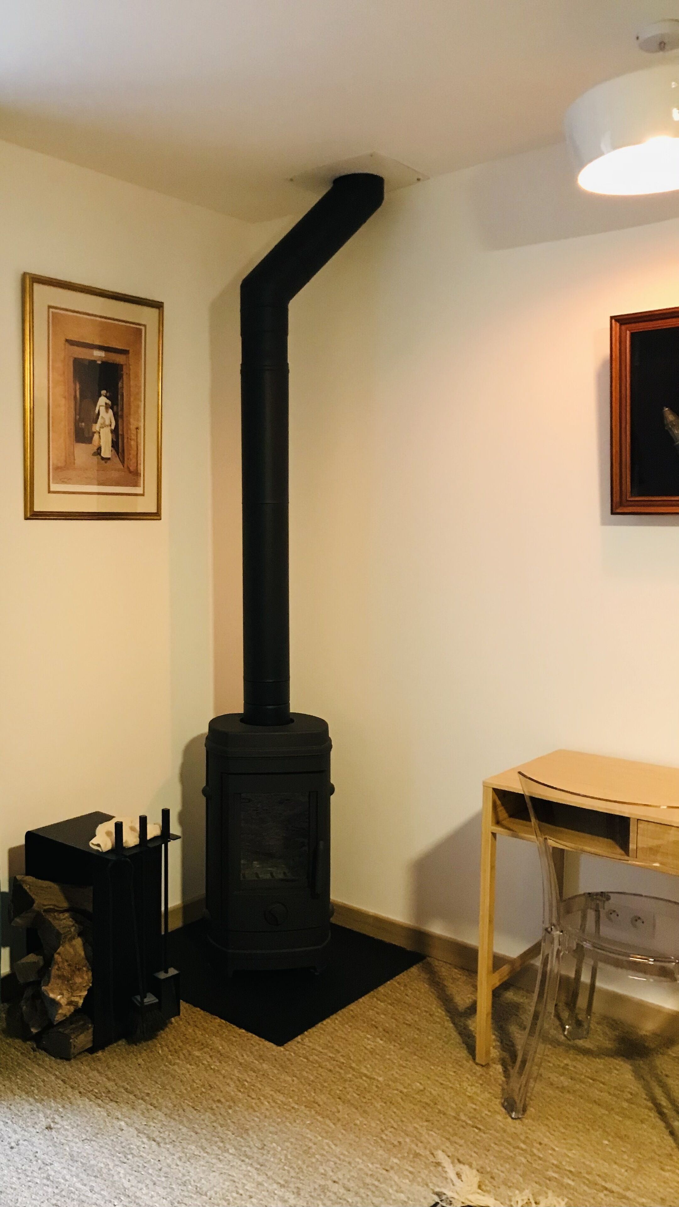 Una habitación con un estufa de leña negra, un cuadro enmarcado en la pared y una mesa de madera.