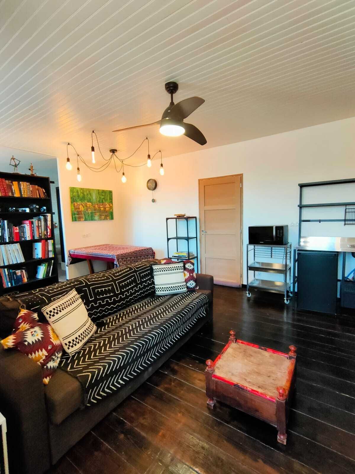 A living room with a sofa, a coffee table, a bookshelf, a painting, a ceiling fan, and a microwave.