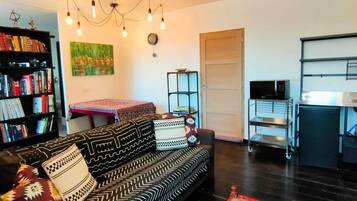 A living room with a sofa, a coffee table, a bookshelf, a painting, a ceiling fan, and a microwave.