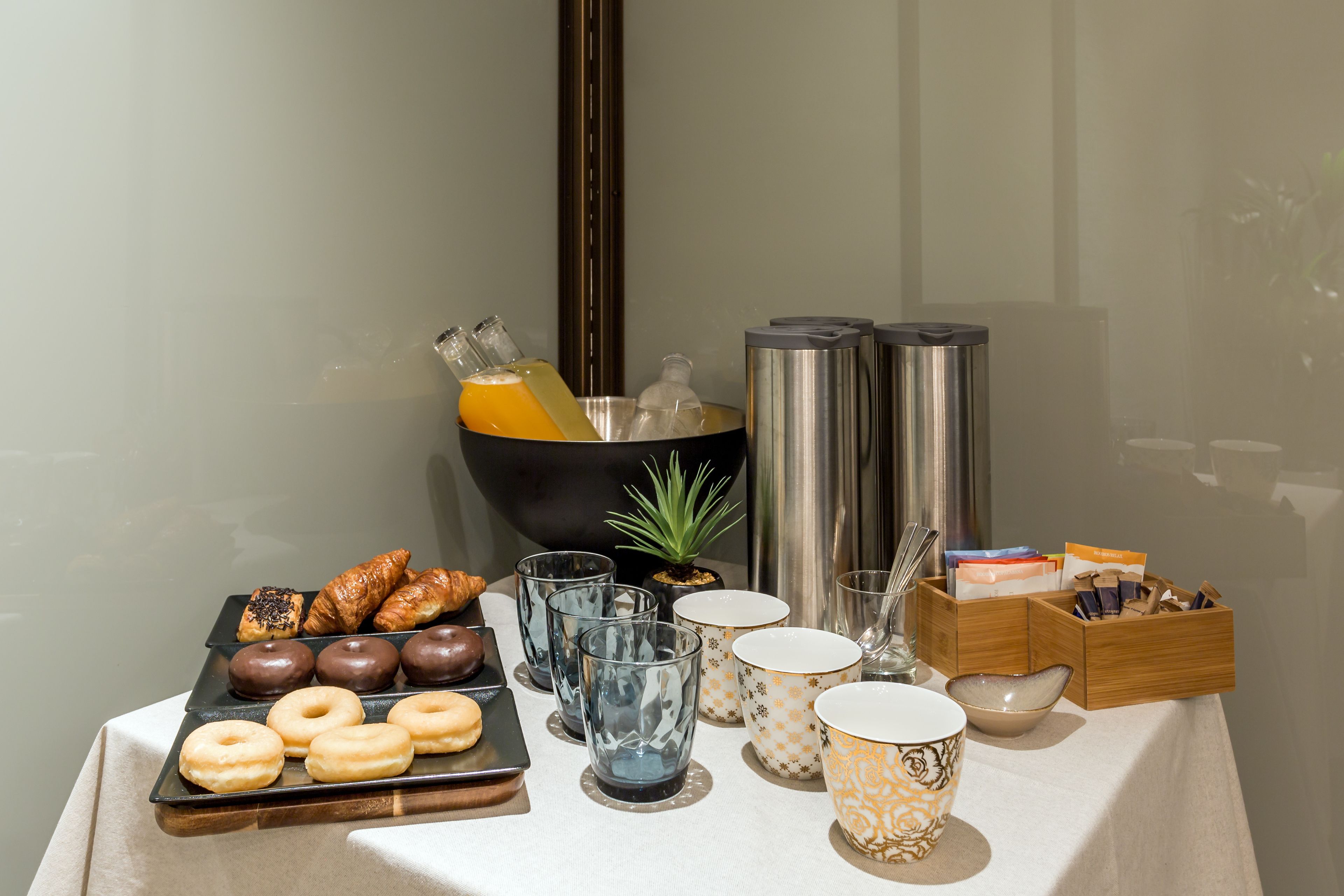 Un bufé de desayuno con pastelería, bebidas y una pequeña planta sobre la mesa.
