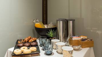 Un bufé de desayuno con pastelería, bebidas y una pequeña planta sobre la mesa.