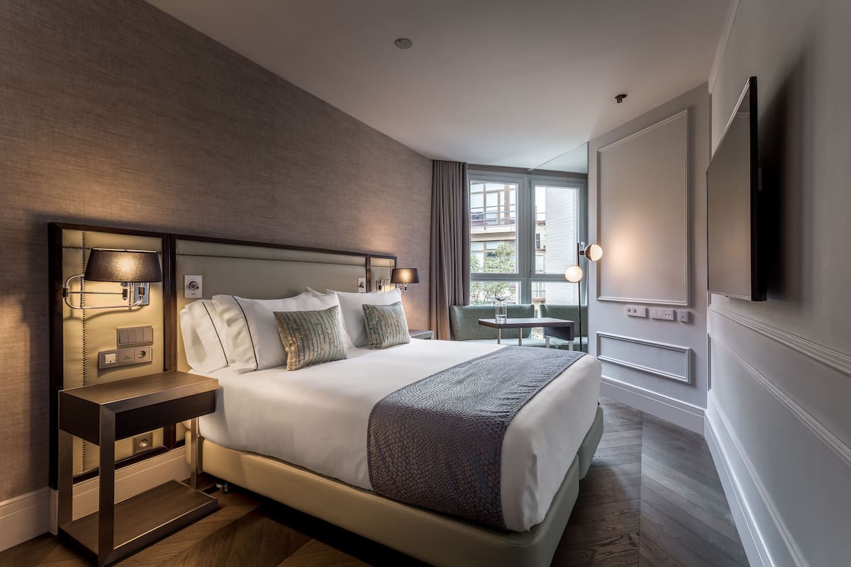 Habitación de hotel moderna con una cama grande, lámparas de noche, un televisor de pantalla plana y vistas al exterior.