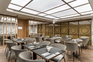 A modern restaurant with a high ceiling and skylight, featuring a marble wall and a circular decorative pattern on the back wall. - Room Mate Collection Gorka, San Sebastián (San Sebastián)