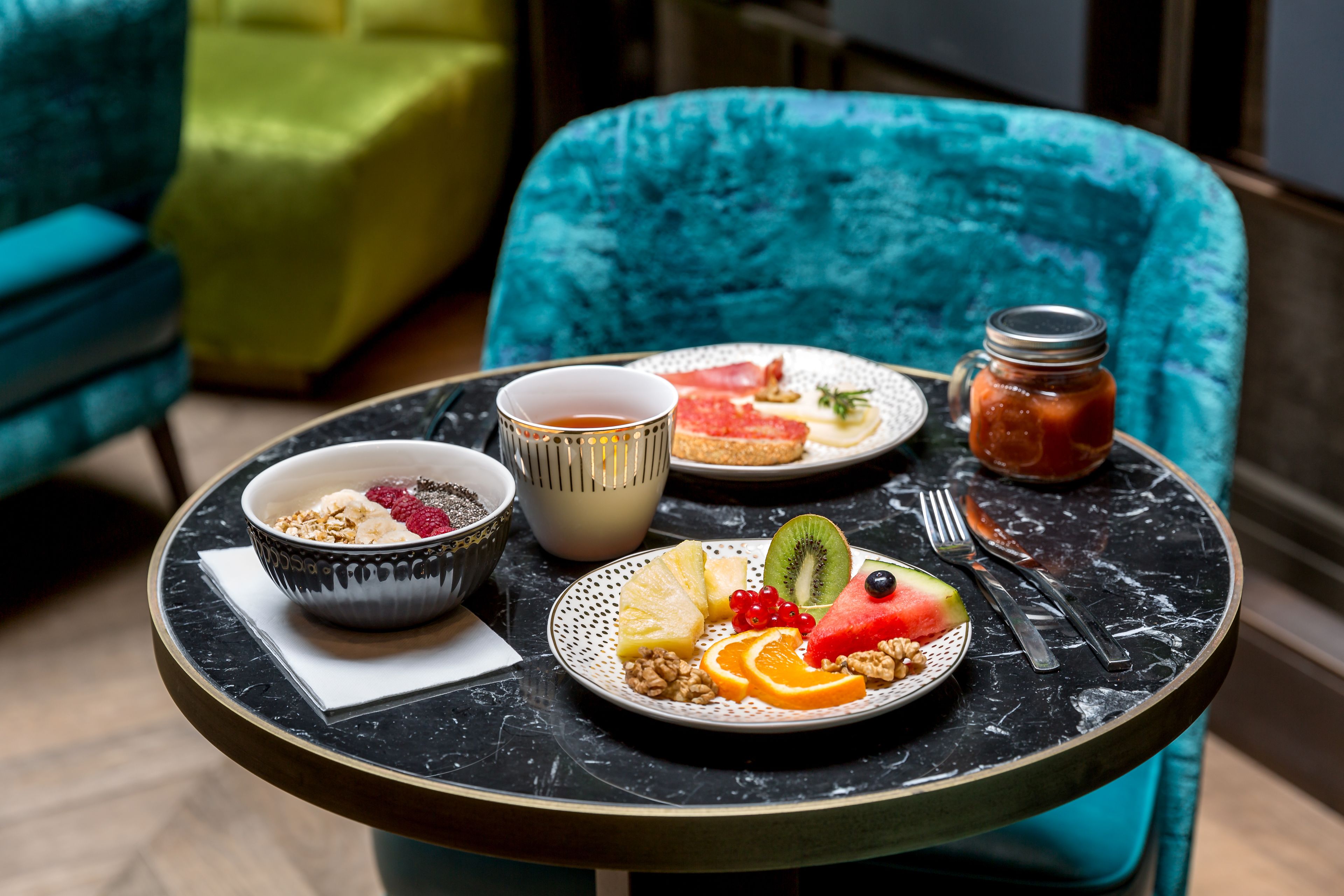 Een eettafel met een bord fruit, een kom ontbijtgranen, een kop en een pot jam.