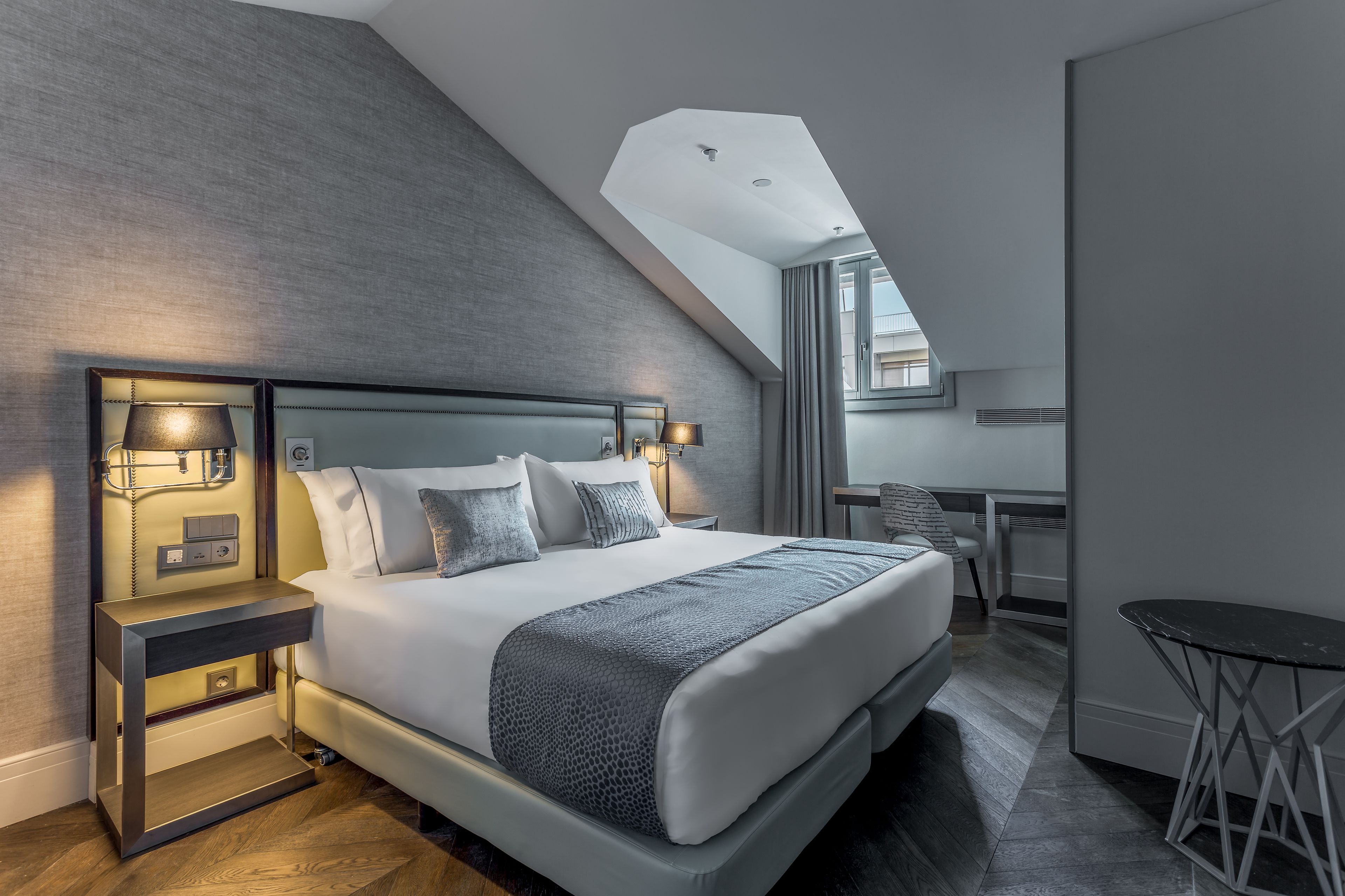 A modern hotel room with a large bed, bedside lamps, a desk, and a small table.