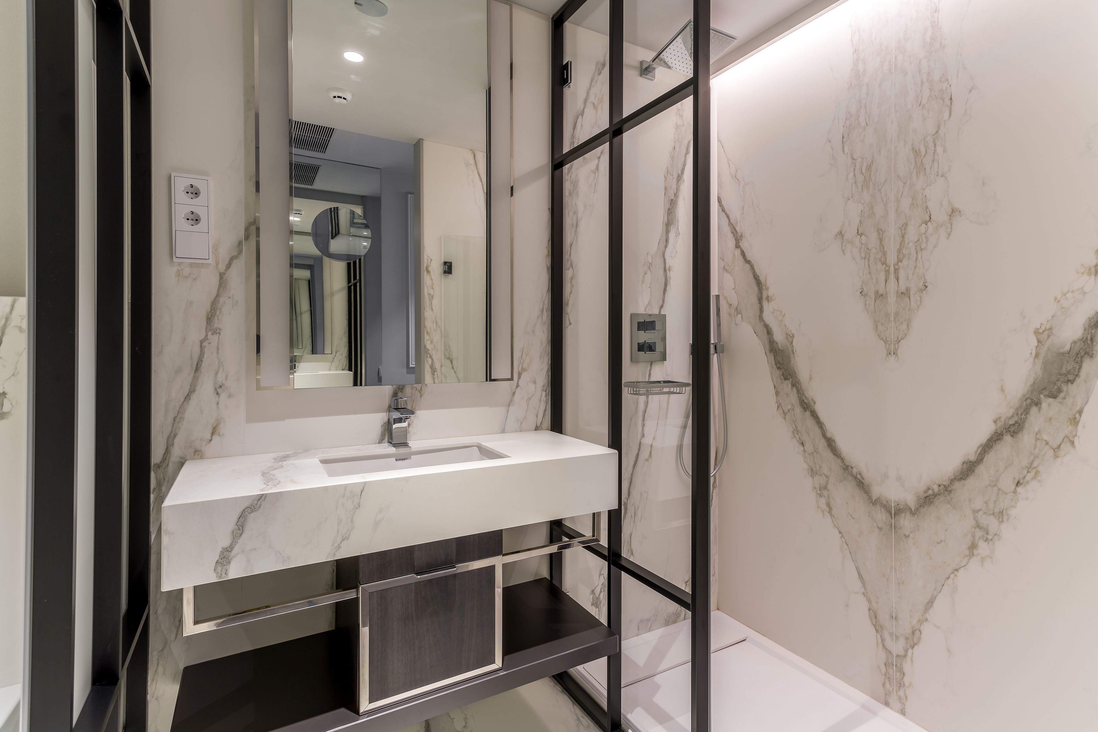 A modern bathroom with a marble sink, a glass-enclosed shower, and a large mirror.