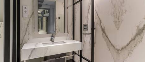 A modern bathroom with a marble sink, a glass-enclosed shower, and a large mirror.