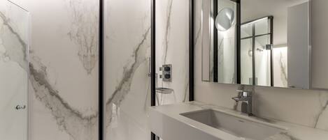 A modern bathroom with a marble wall, a glass shower enclosure, and a large mirror.