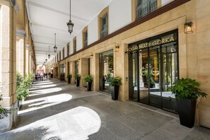 A corridor with a storefront named "ROOMATE GORKA," featuring a modern design with large windows and potted plants. - Room Mate Collection Gorka, San Sebastián (San Sebastián)