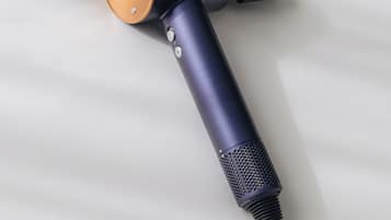 Un secador de pelo con mango negro y punta naranja, sobre una superficie blanca.