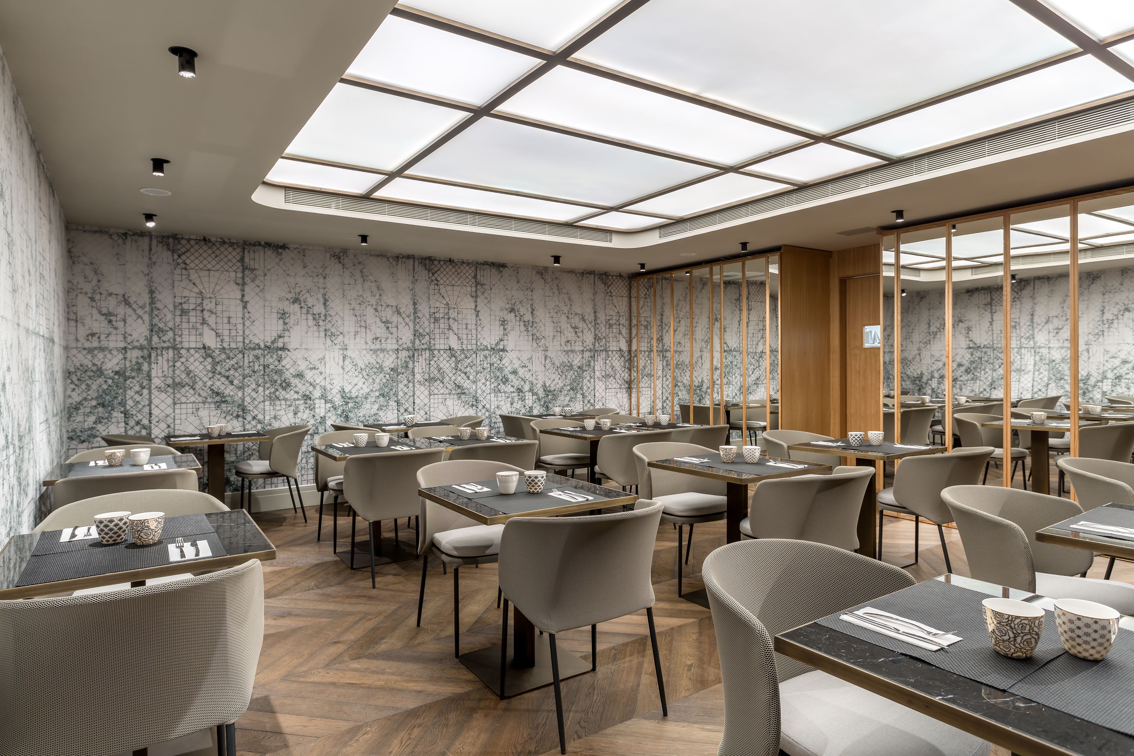 Ein modernes Restaurant mit hohen Decken und Oberlichtern, Wänden im Marmor-Design und verschiedenen Sitzmöglichkeiten.