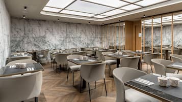 Ein modernes Restaurant mit hohen Decken und Oberlichtern, Wänden im Marmor-Design und verschiedenen Sitzmöglichkeiten.
