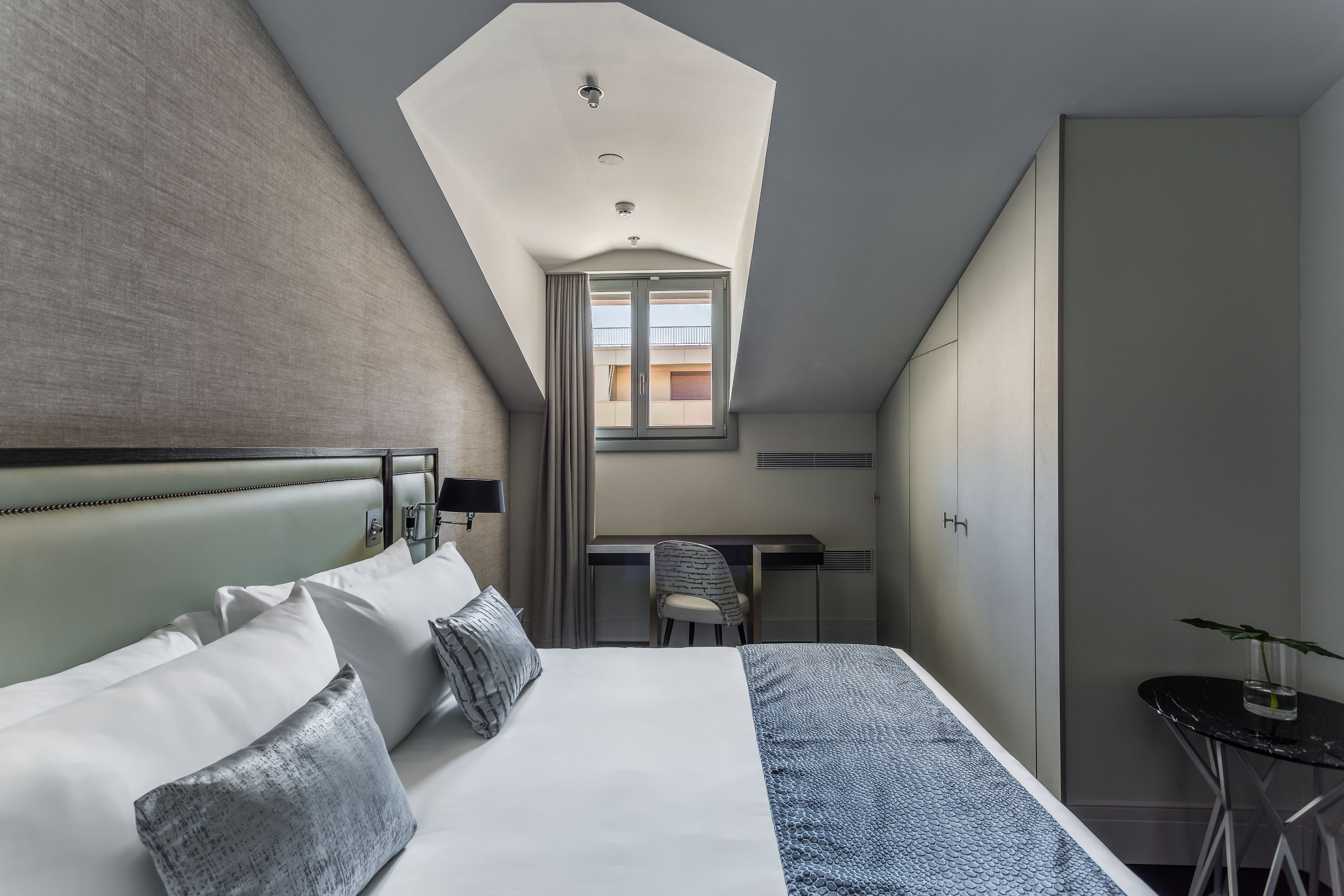 A modern hotel room with a large bed, a desk, and a skylight.