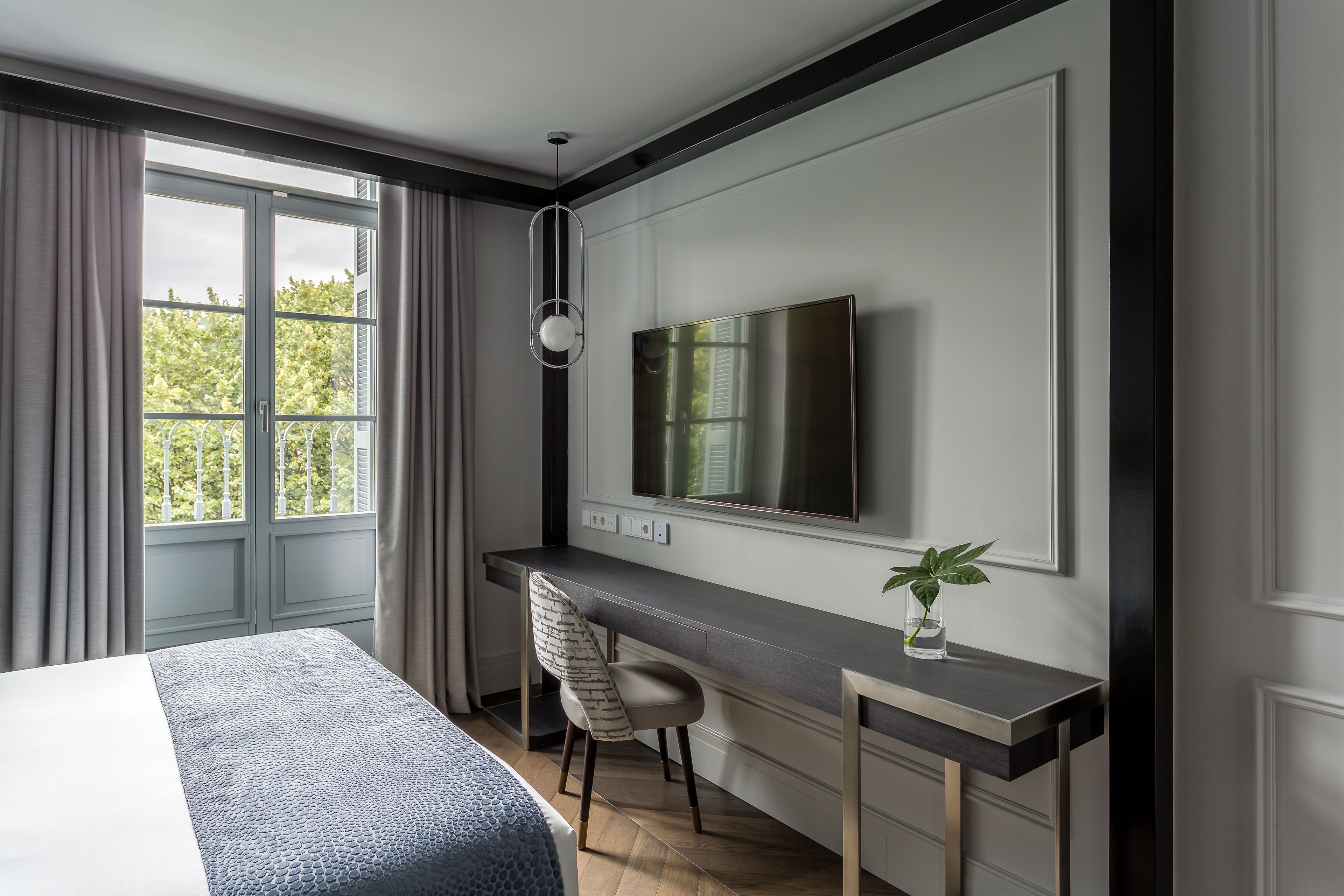 A modern hotel room with a large bed, a desk, and a TV mounted on the wall.