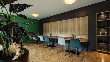 Zona pranzo moderna con tavoli e sedie in legno, un'ampia parete d'accento in legno e una pianta in vaso con foglie scure.