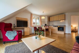 A modern apartment with a dining area, kitchen, and a red armchair with a heart-shaped throw.
