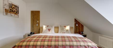 A bedroom with a large bed, wooden headboard, and a sloped ceiling.