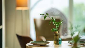 Une table à manger avec une assiette verte, un vase contenant une plante et un verre.