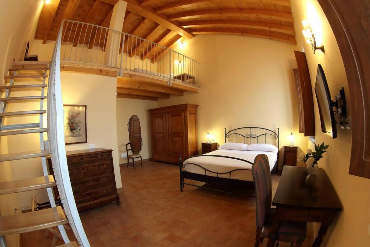 A bedroom with a wooden ceiling, a bed, a desk, a chair, a dresser, and a staircase.