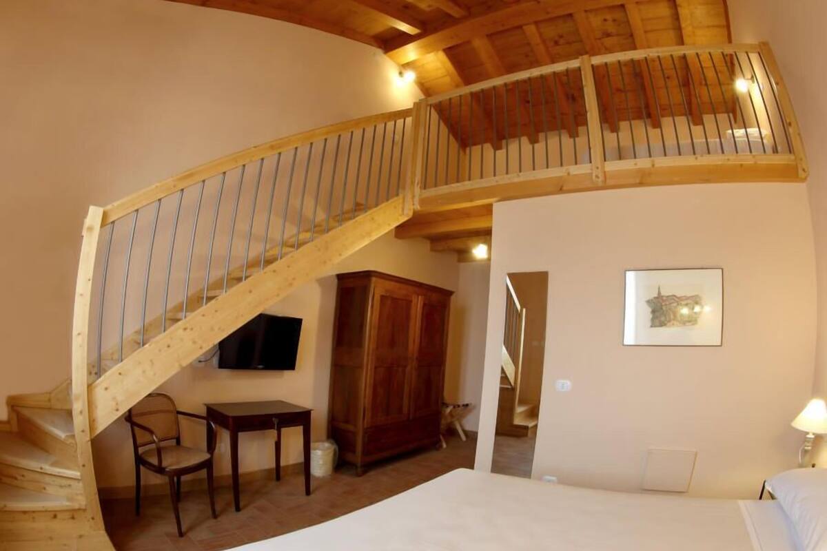 A bedroom with a wooden staircase, a bed, a desk, a chair, and a wardrobe.