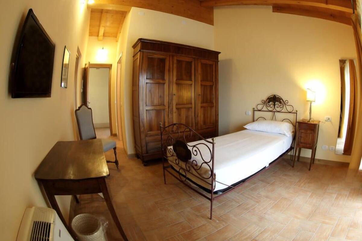 A bedroom with a bed, a wooden wardrobe, a desk, and a chair.