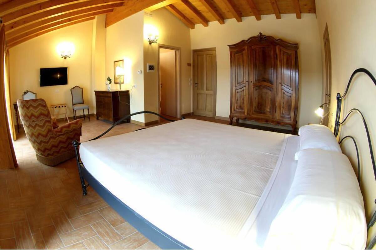 A bedroom with a large bed, wooden ceiling beams, a wooden wardrobe, and a chair.