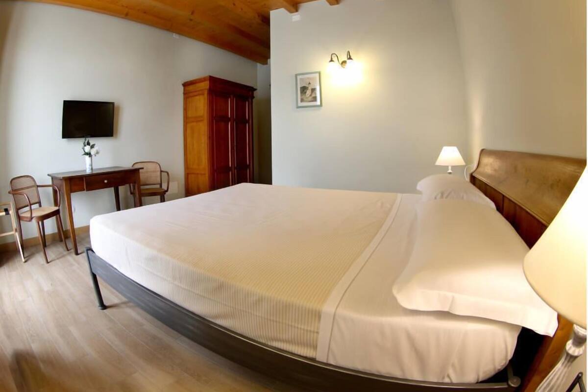 A bedroom with a large bed, a desk with a chair, a wardrobe, and a wall-mounted TV.