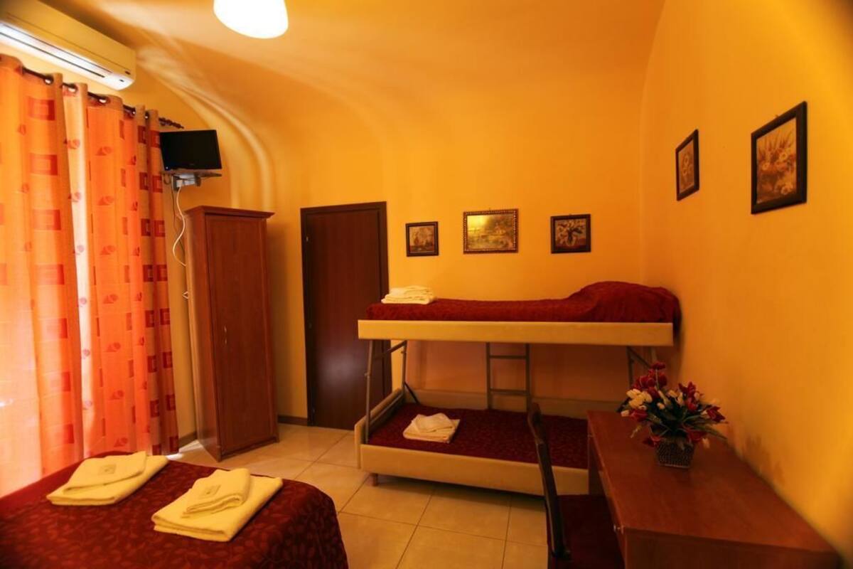 A small, compact room with a bunk bed, a desk, a chair, and a small table with a vase of flowers.