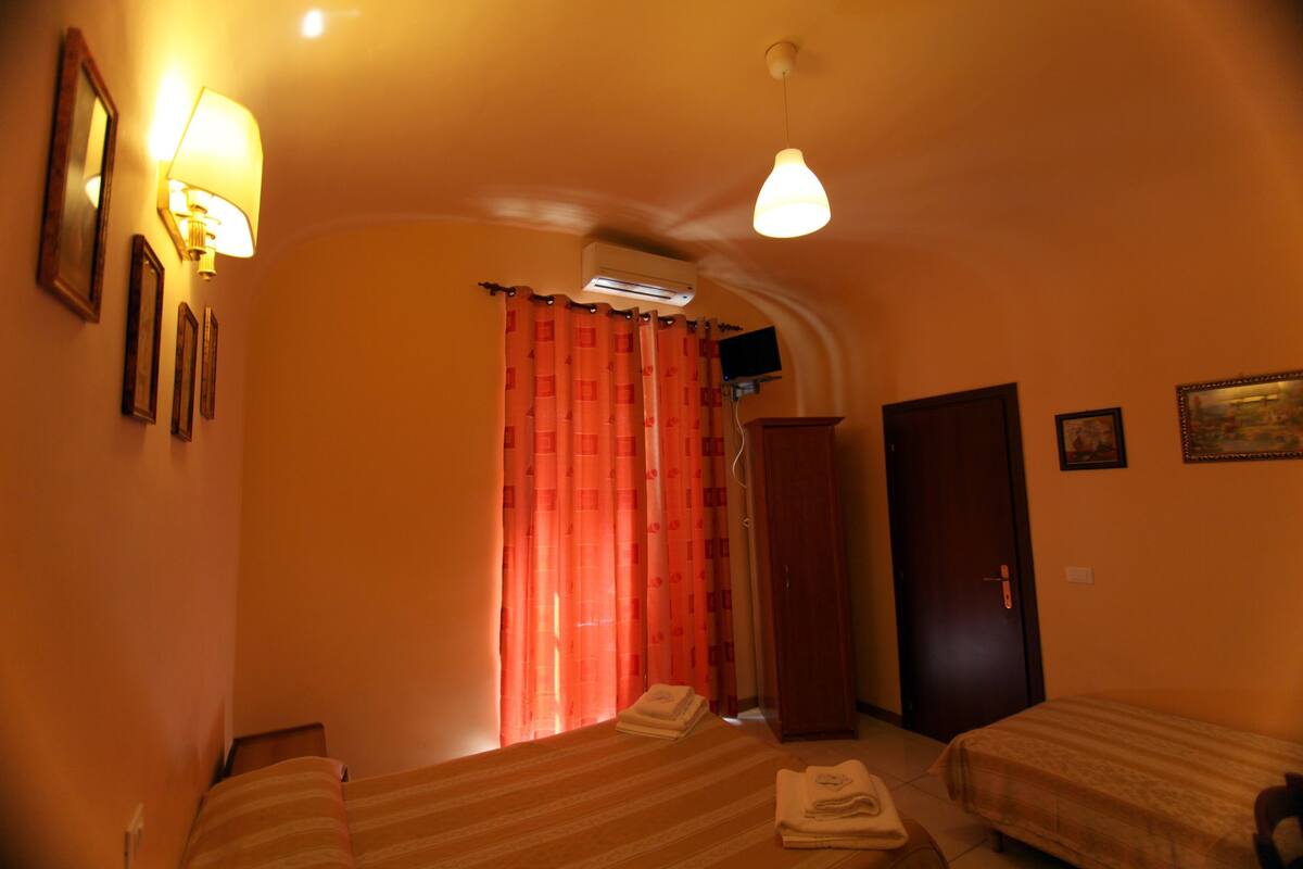 A hotel room with two beds, a wardrobe, a desk, and a television.