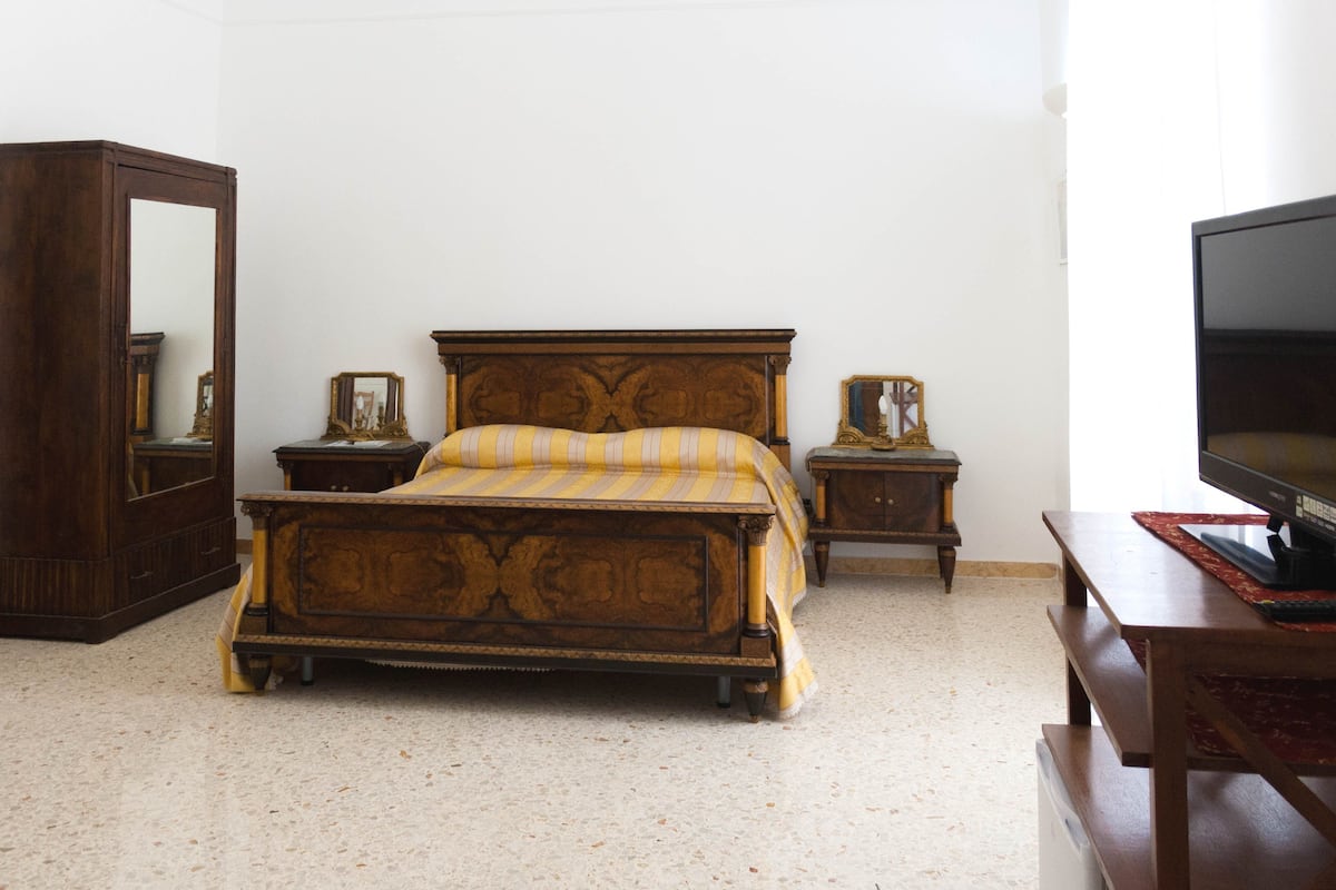 Un dormitorio con una cama grande de madera, un aparador de madera, un televisor y un espejo.