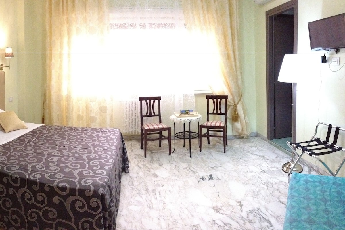 Ein Hotelzimmer mit Bett, zwei Sesseln, einem kleinen Tisch, einem Fernseher und einem Bild an der Wand.