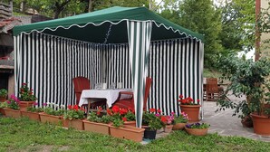 A covered outdoor seating area with a striped canopy, a table set for two, and potted plants around the perimeter. - Cherry House B&B (Polinago)