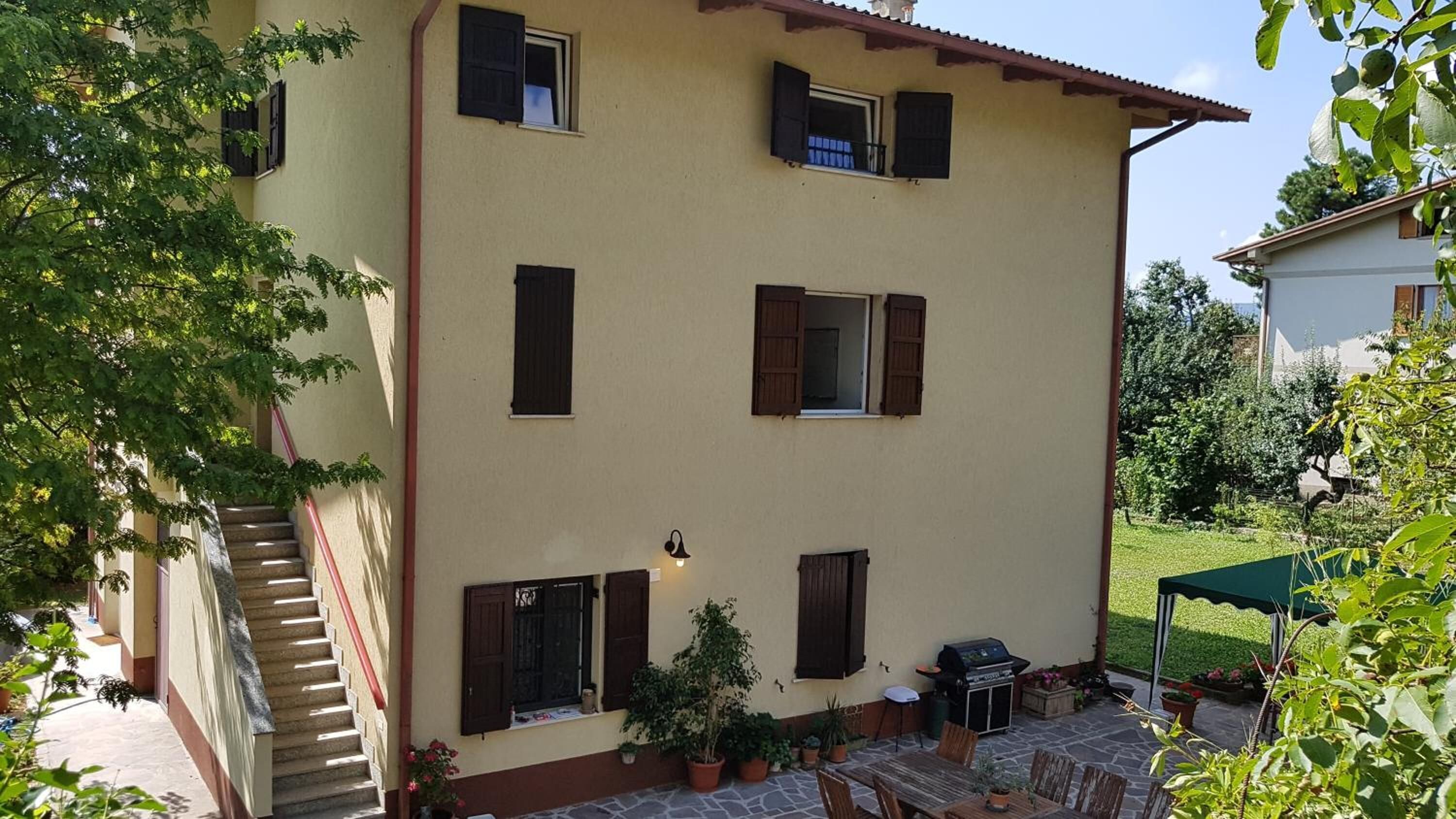 A two-story building with multiple windows, a staircase, outdoor seating, and a barbecue grill.