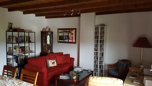 A living room with a red sofa, a wooden coffee table, a bookshelf, a tall bookcase, and a lamp. - Cherry House B&B (Polinago)
