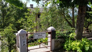 A gated entrance with a sign for Cherry House B&B, surrounded by lush greenery and a building in the background. - Cherry House B&B (Polinago)