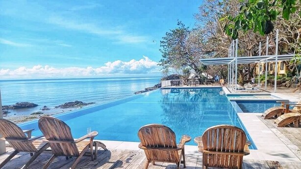 Zona de piscina con sillas de madera y vista al océano.