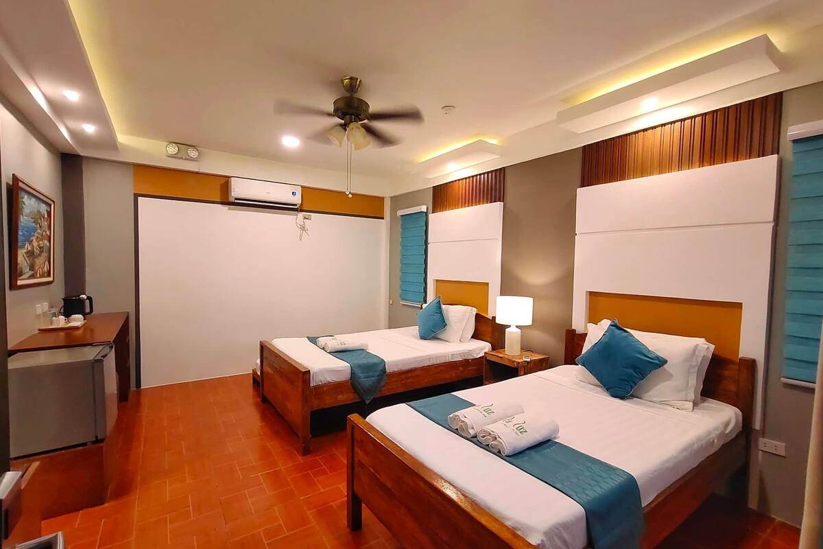 Una habitación de hotel con dos camas, un escritorio, un aire acondicionado y un ventilador de techo.