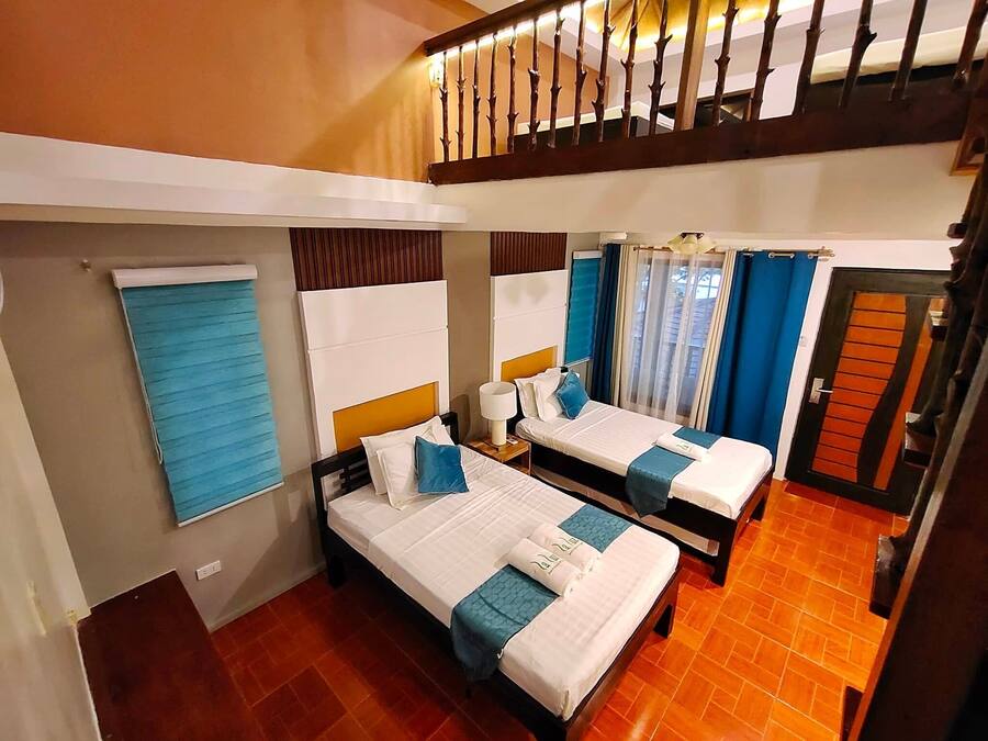 A hotel room with two beds, a window with blinds, a wooden staircase, and a door with a unique design.